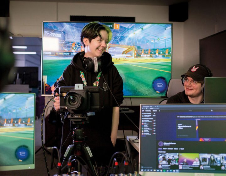 Esports students stood in front of digital screens with cameras